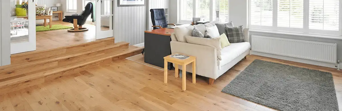 A modern living room with professionally installed laminate flooring, a beige sofa, a small side table, a gray rug, and large windows with white shutters in Tuscaloosa, AL
